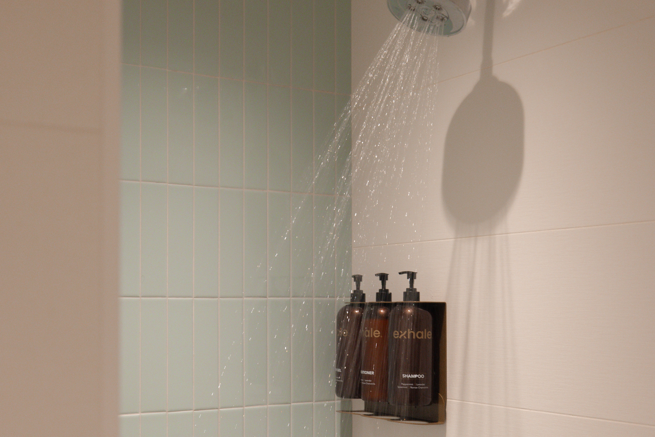Shower with water flowing, featuring exhale-branded shampoo and conditioner bottles on a wall, in a wellness spa setting.