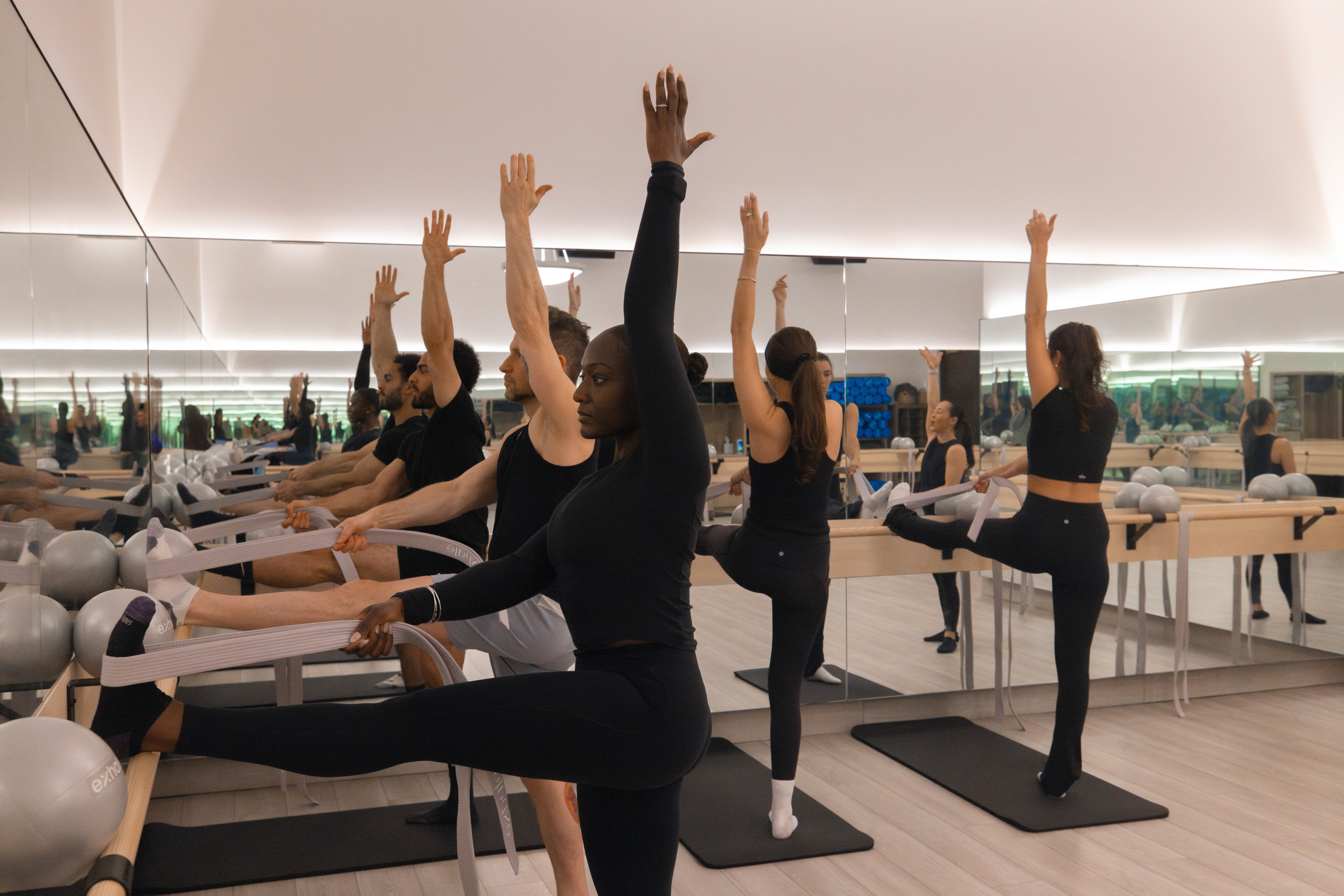 Group of individuals participating in a fitness class, performing stretches and exercises with resistance bands in a modern studio environment, emphasizing wellness and fitness at Exhale Spa.