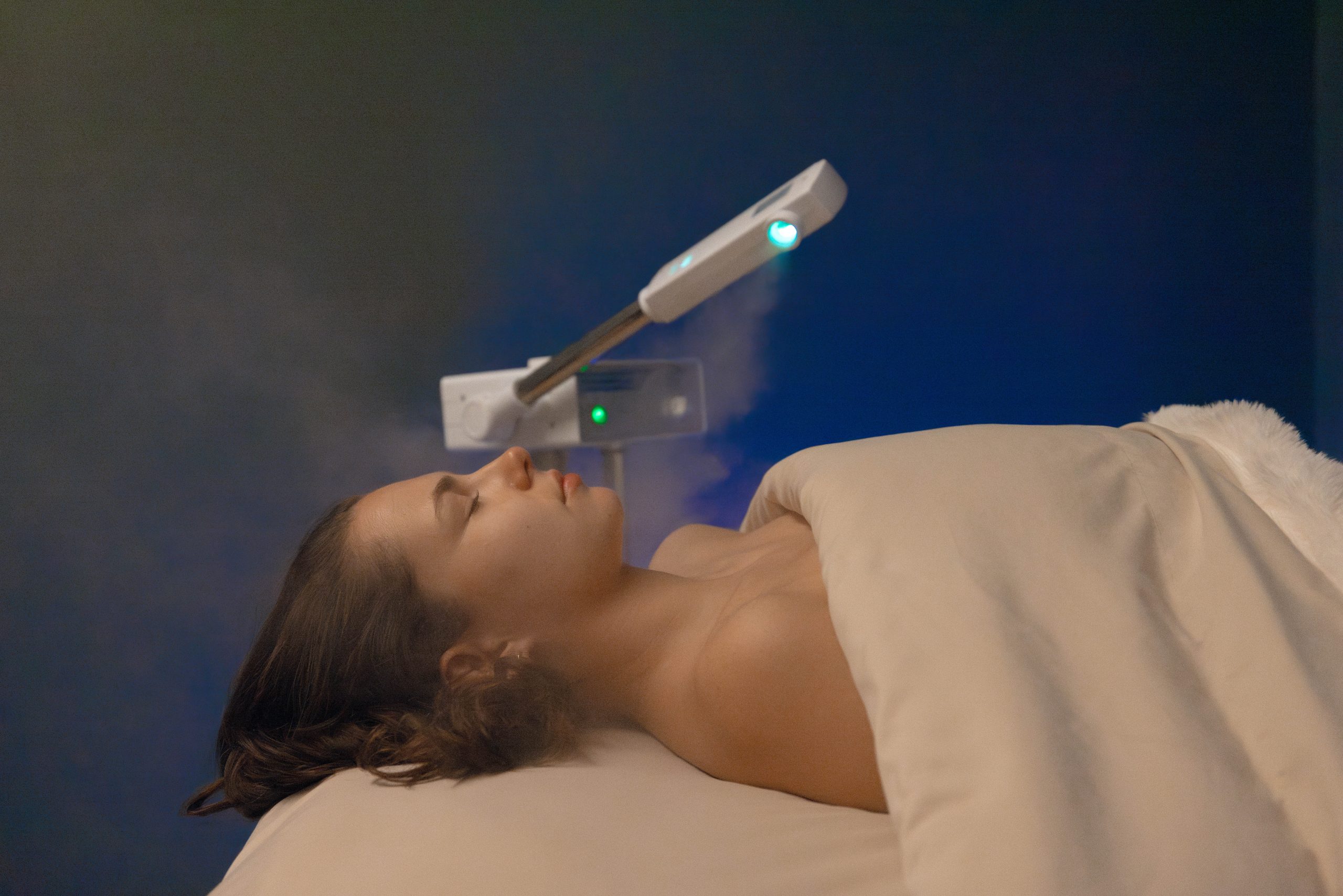 Woman receiving a facial treatment with a steam device in a serene spa environment, emphasizing wellness and relaxation at Exhale Spa, Central Park.