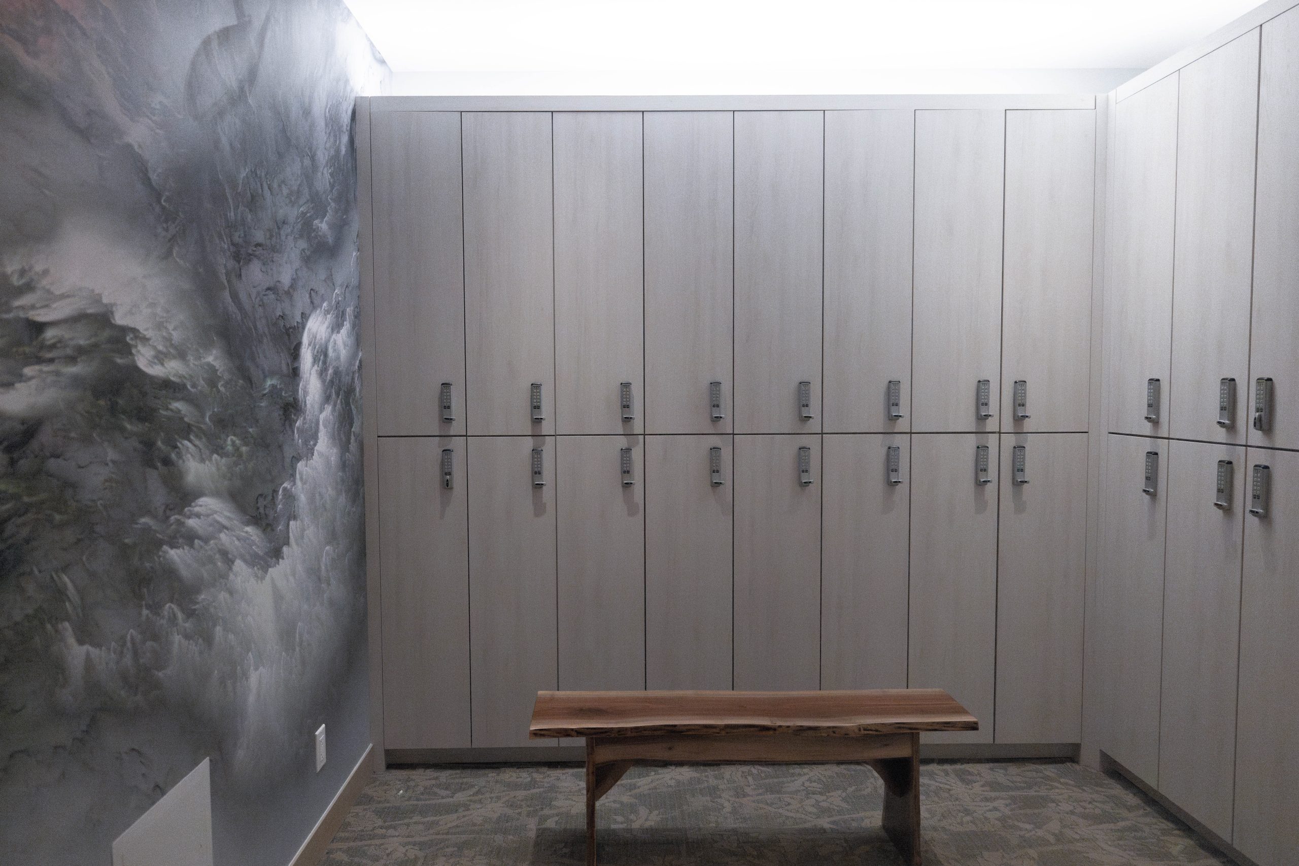 Spa locker room with wooden benches, modern lockers, and abstract wall mural, reflecting Exhale Spa's wellness environment at Thompson Central Park.