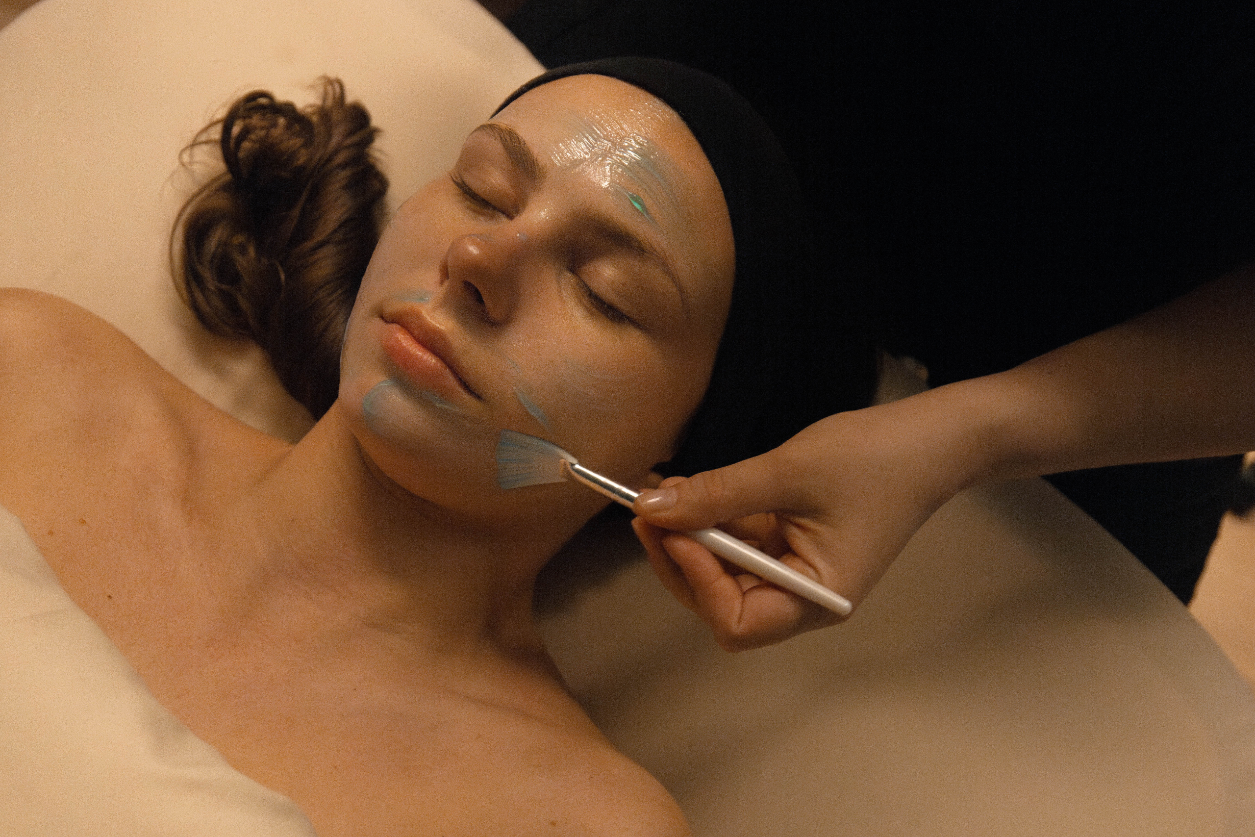 Woman receiving a facial treatment at a spa, with a therapist applying a blue mask on her face, emphasizing relaxation and skincare services offered at Exhale Spa in Central Park.