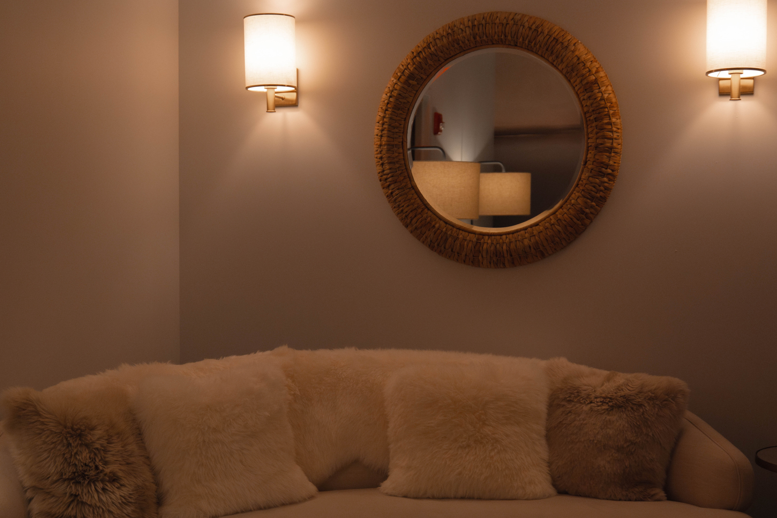 Tranquil spa lounge area with plush fur pillows, warm wall sconces, and a circular mirror, reflecting a serene ambiance at Exhale Spa, Thompson Central Park.