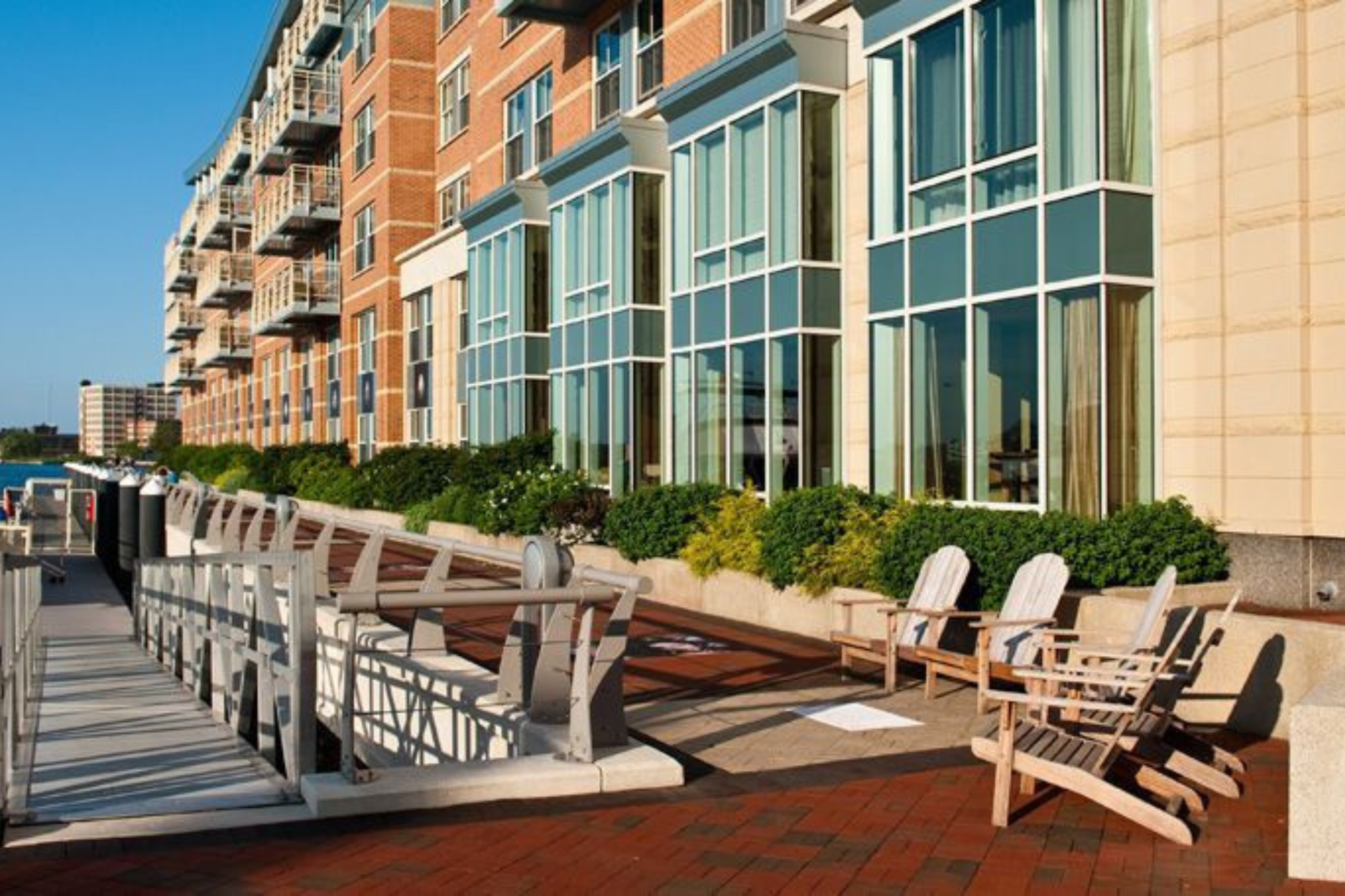 Boston waterfront view of Exhale Spa's luxurious outdoor seating area with wooden chairs, landscaped greenery, and modern building architecture.