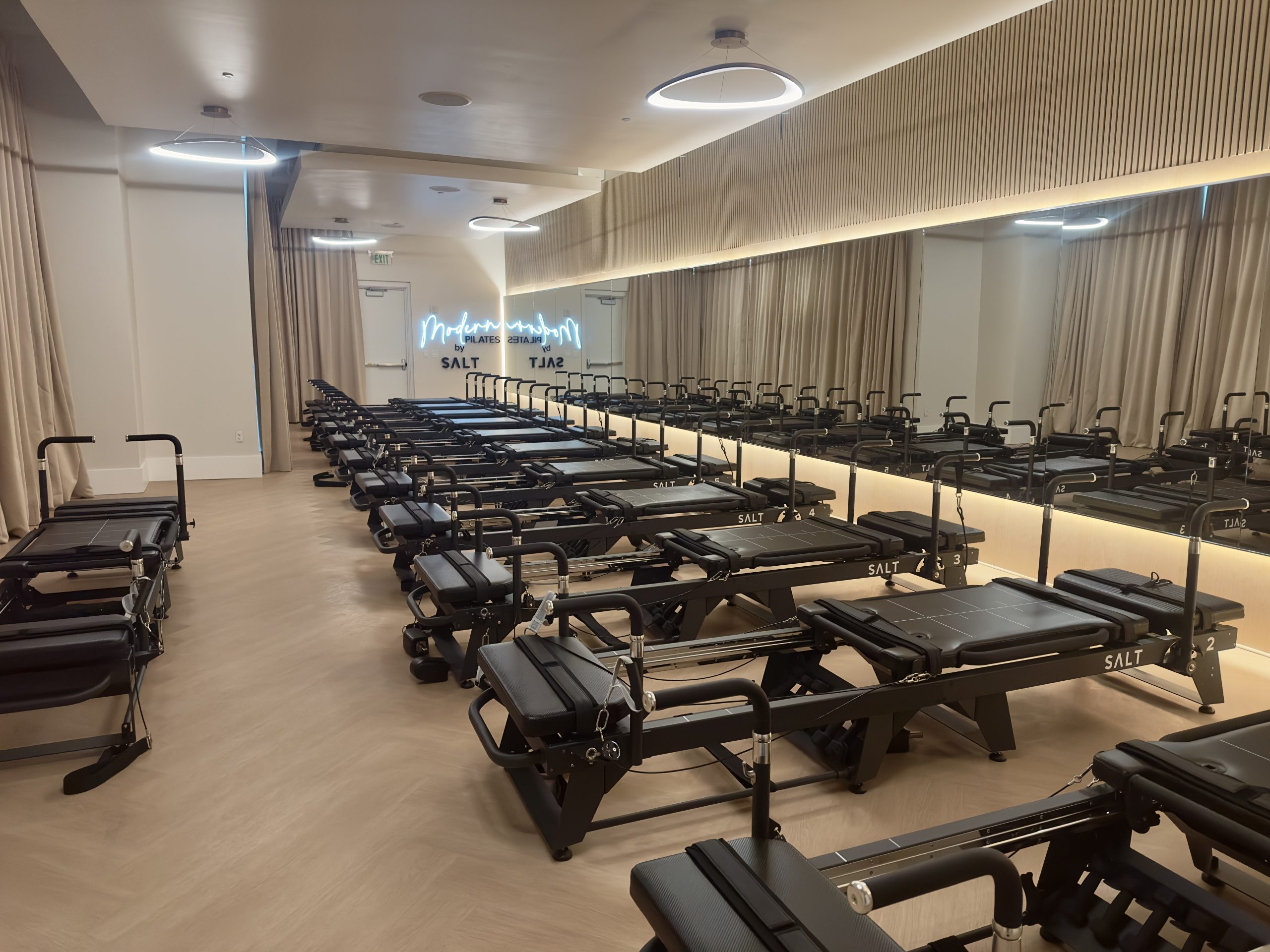 Modern Pilates studio featuring multiple reformers, sleek design, and illuminated "Modern Pilates by SALT" sign, emphasizing fitness and wellness offerings at exhale spa in Atlanta.