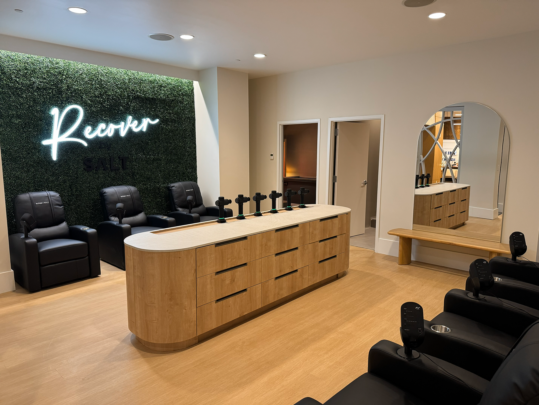 Wellness spa recovery area featuring "Recover" neon sign, massage chairs, and a service counter with recovery equipment, designed for relaxation and rejuvenation at exhale spa in Atlanta.