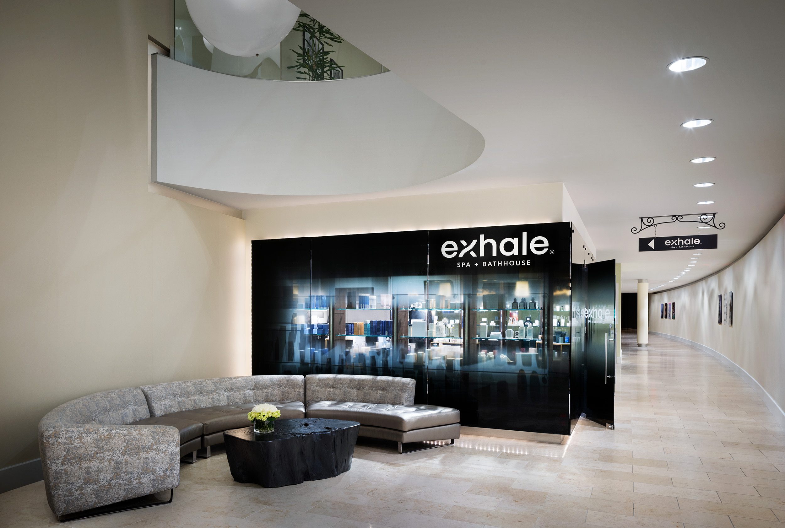 Exhale Spa entrance featuring a modern reception area with curved seating, a dark display cabinet showcasing wellness products, and a sign directing to the spa in Atlantic City.