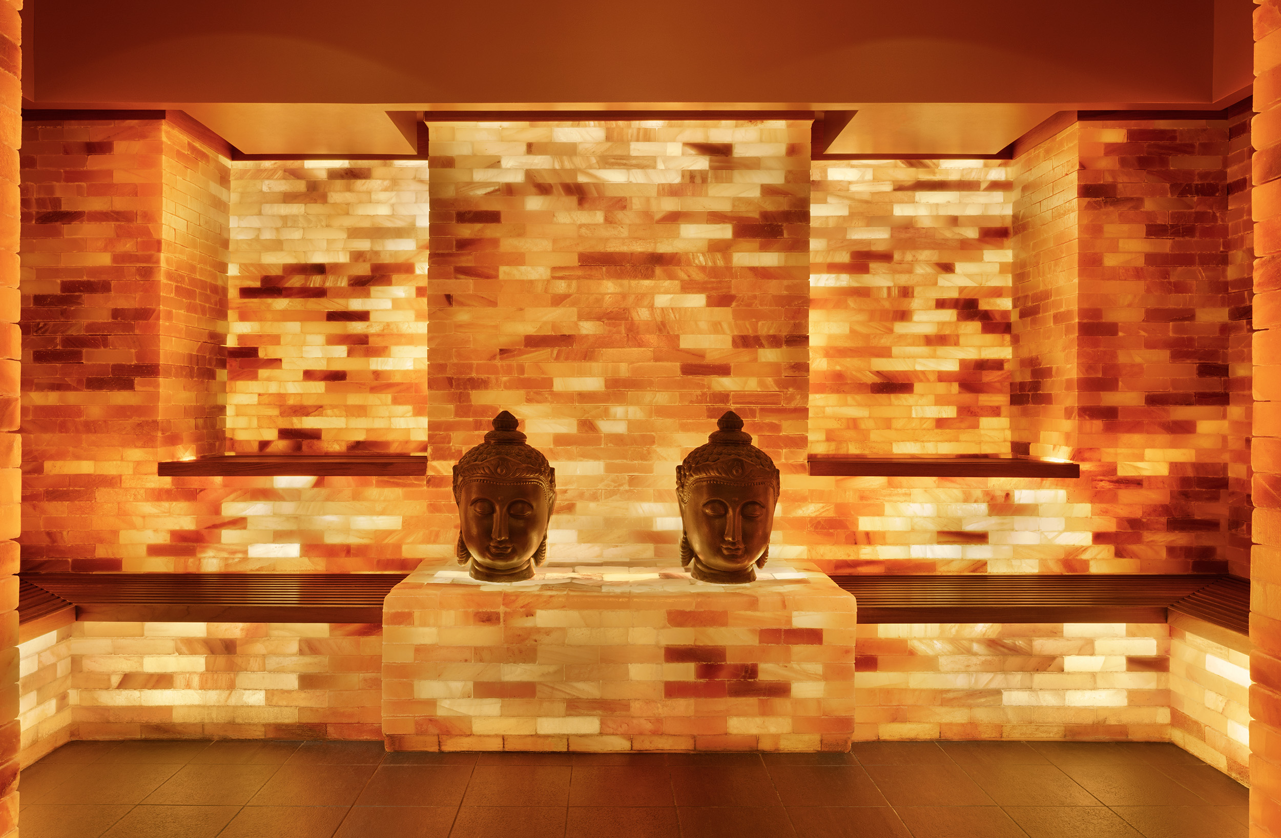 Salt room with illuminated Himalayan salt walls and two decorative Buddha heads, creating a serene atmosphere for wellness and relaxation at Exhale Spa in Atlantic City.