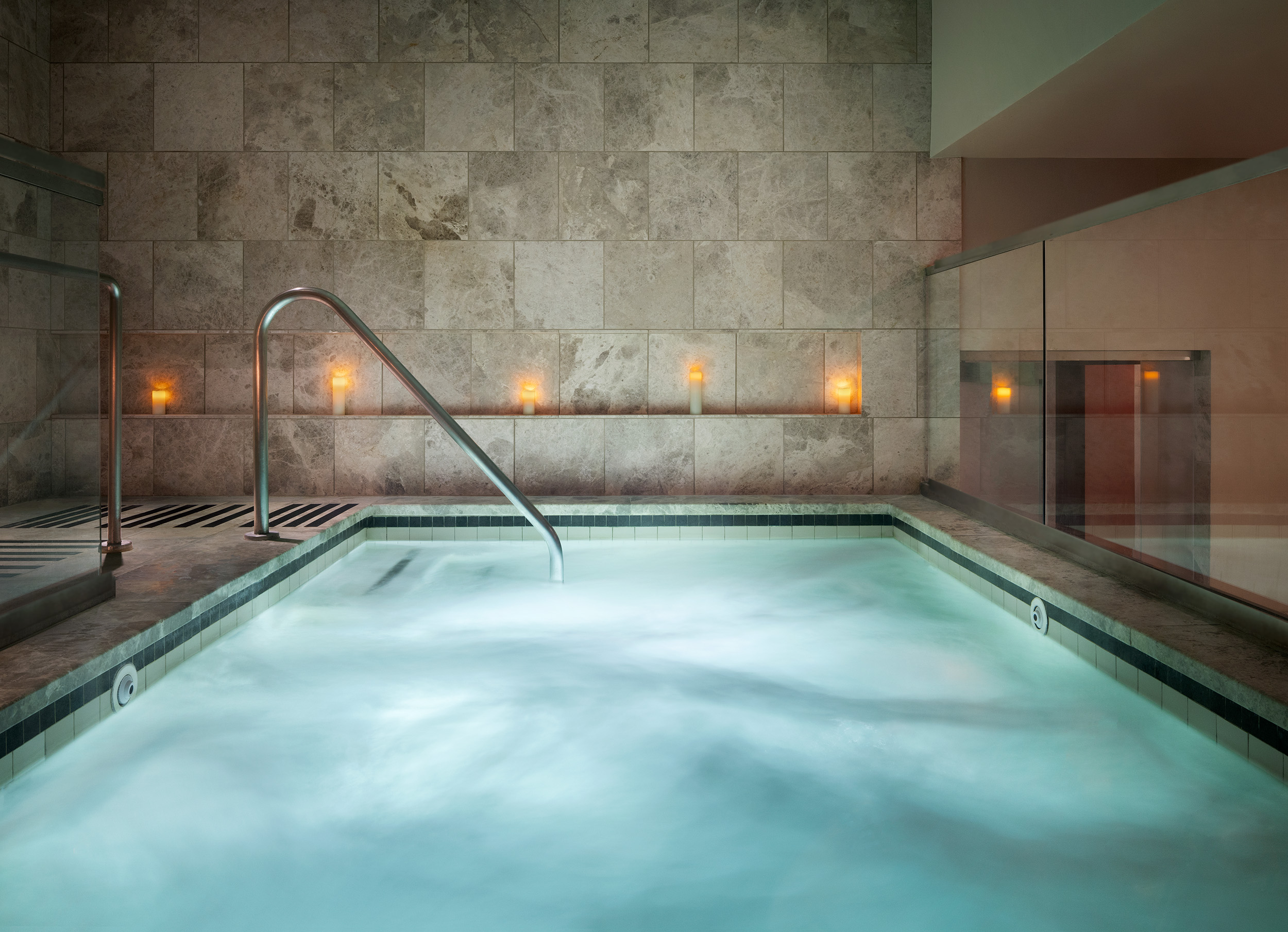 Luxurious spa jacuzzi with soothing water, candlelit ambiance, and elegant stone walls at Exhale Spa in Atlantic City, promoting relaxation and wellness.